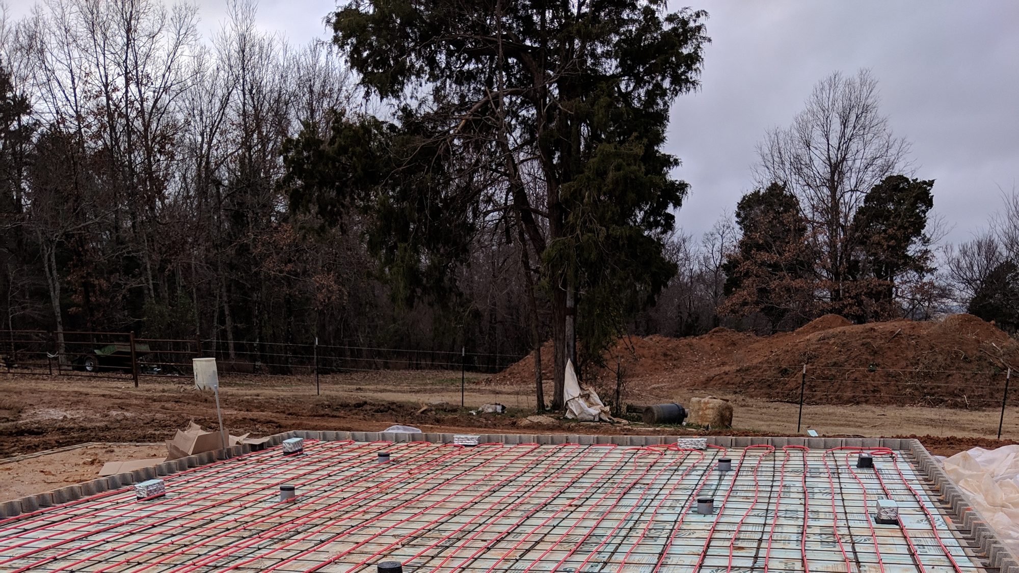 Red PEX radiant floor heating tubing laid across a rebar-reinforced foundation slab before the pour