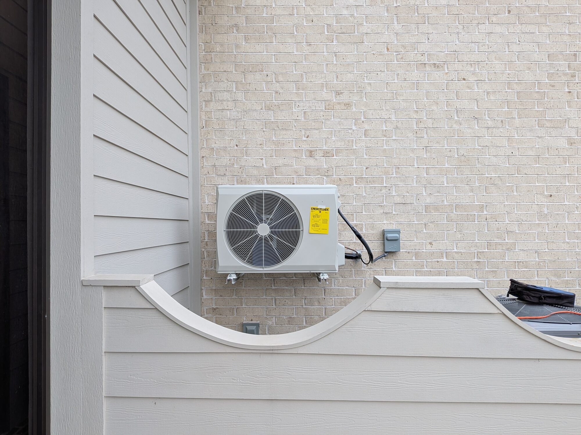 Carrier mini-split outdoor unit on wall brackets against a brick wall, tucked behind a privacy screen