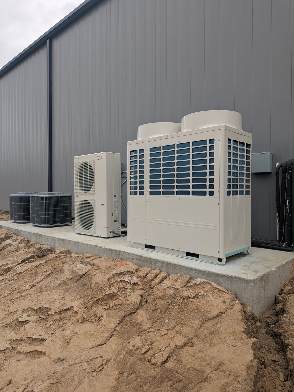 VRF condensing units and residential condensers installed outside a large commercial building under construction